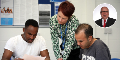 Photo of a woman with a lanyard leaning over two men concentrating and reading pieces of paper in an office setting